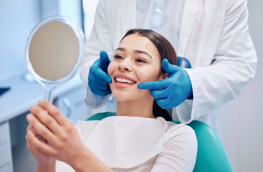Woman smiling and looking into a mirror after a dental cleaning.