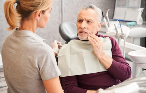 An elderly man talking with his dentist about his severe tooth pain in need of treatment