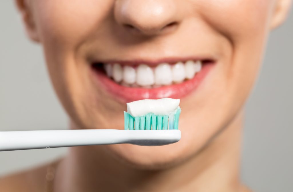 A woman smiling behind a toothbrush she is holding out in front of her face with whitening tooth applied on the bristles