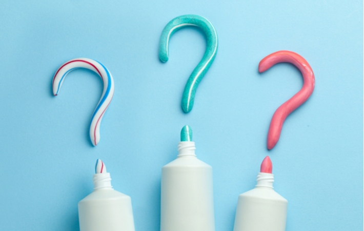 3 tubes of toothpaste that were used to create the shape of 3 corresponding question marks above the tubes on a blue background, to signify the concept of choosing the correct whitening toothpaste