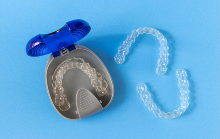 Two sets of Invisalign, one set resting in a container and the other resting on the blue background