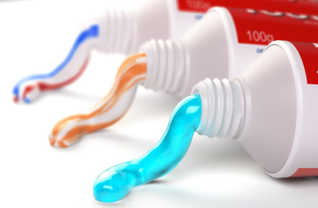 Three different tubes of toothpaste laying on a white surface, all with different colour toothpaste coming out