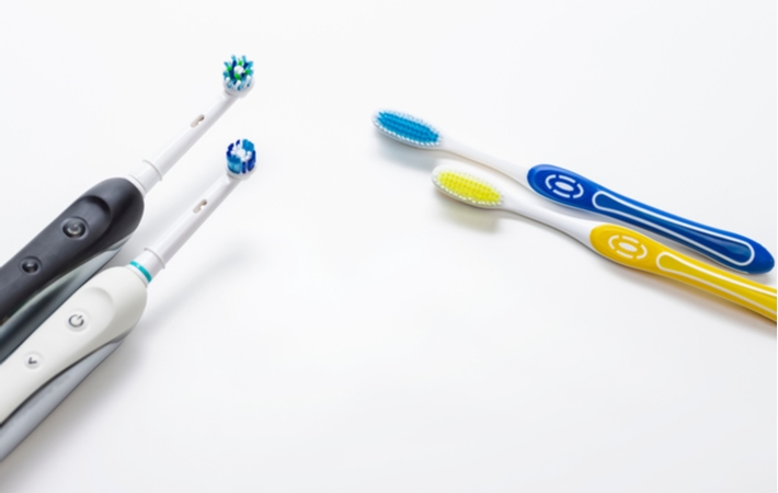 Two pairs of electric toothbrushes and manual toothbrushes positioned beside each other on a white surface