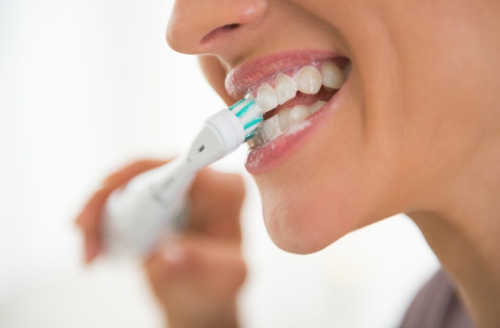 A close-up of a woman brushing her teeth with an electric toothbrush
