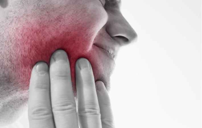 A man holding his cheek that is highlighted in red to illustrate the pain he is experiencing from his tooth