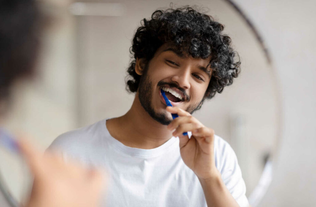male brushing his teeth in the mirror to protect his teeth from plaque and tartar buildup.