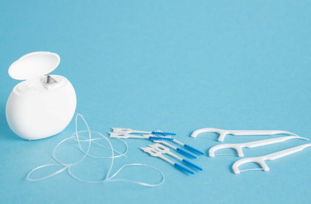 A container of floss, interdental brushes, and floss picks sitting on a blue surface
