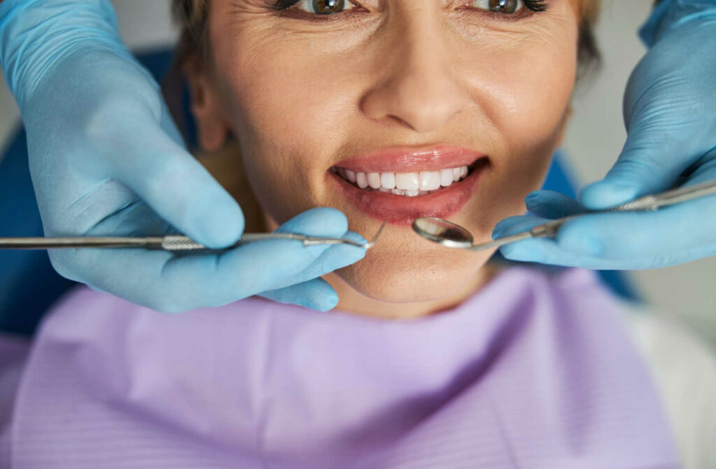 A close up of a patient and the hands of a dentist holding dental tools during a dental exam and cleaning