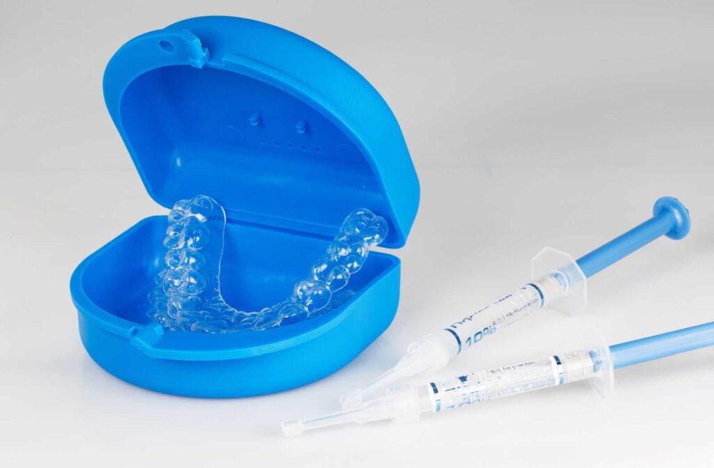 An at-home teeth whitening kit consisting of a container, trays, a whitening gel laying on a white surface.