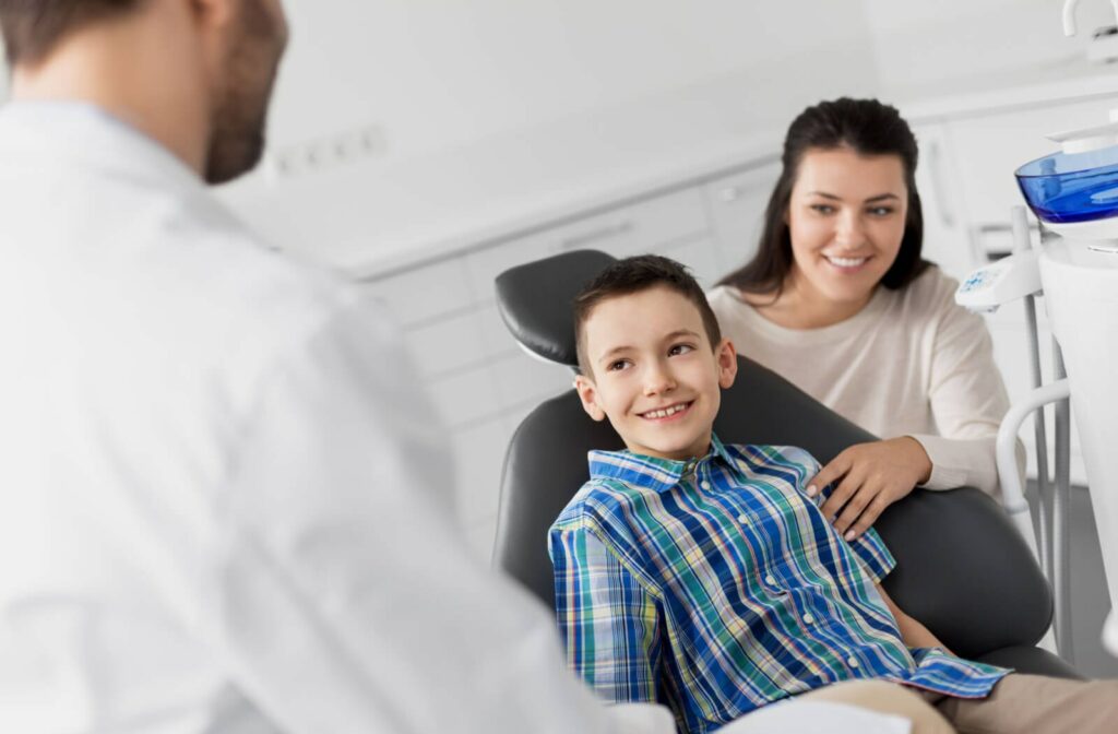 A child sitting in the dentist office smiling to a male dentist with his mother on his side