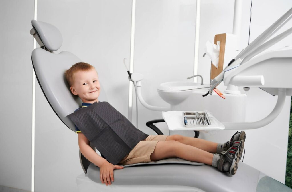 A child with dental bib sitting in the dentist office, smiling and looking directly at the camera
