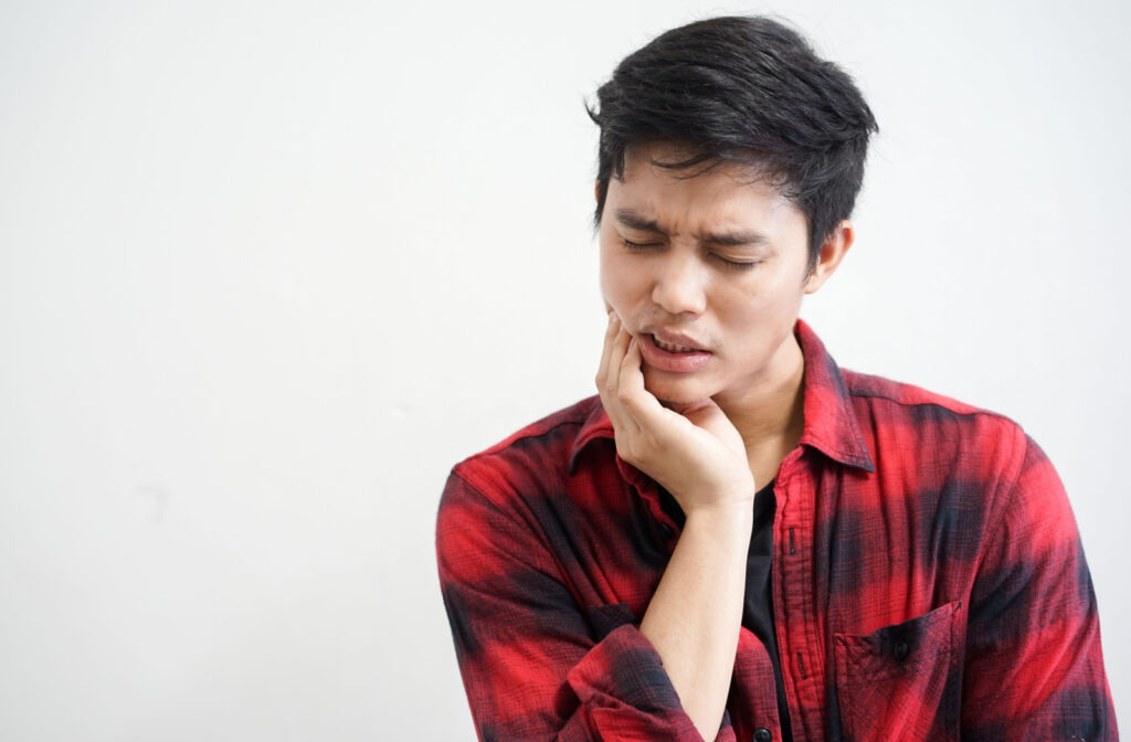 A young man in a plaid shirt applying pressure to his jaw to alleviate pain caused by an impacted wisdom tooth.