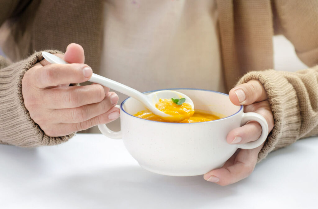 Close-up of a person's hands holding and scooping a spoonful of butternut squash soup to eat after wisdom teeth removal.