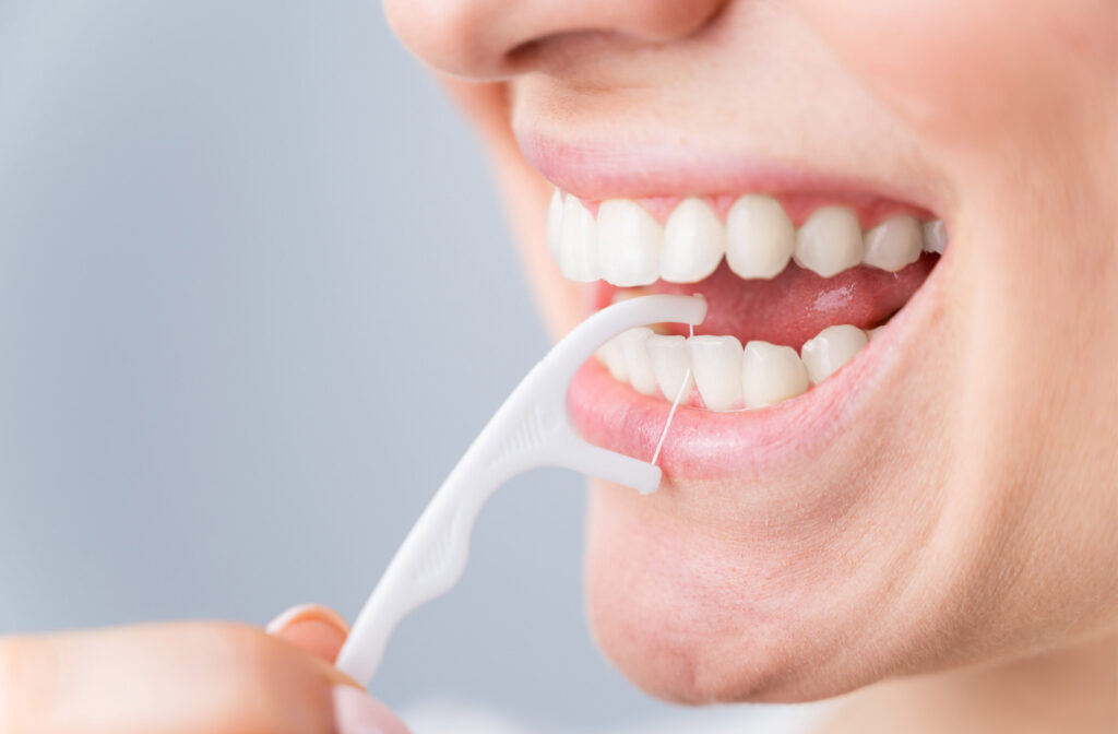 A close up of a person using a floss stick in between their teeth to prevent plaque build up, cavities, and gum disease.