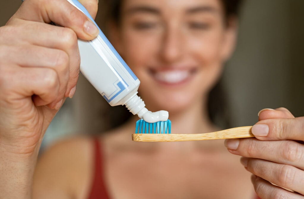 A woman smiling and applying a toothpaste on a toothbrush.