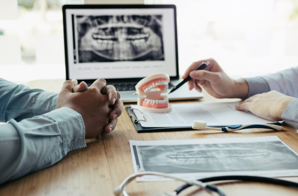 A close-up of a dentist using a pen to gesture to a model of a patient's teeth while explaining what to expect from their dental costs.