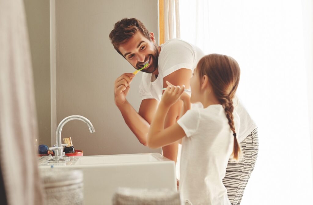 A father and daughter brushing their teeth in the mirror to avoid tooth sensitivity.