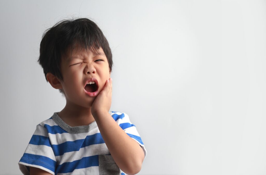 A child holding their cheek and wincing in pain from a chipped tooth.