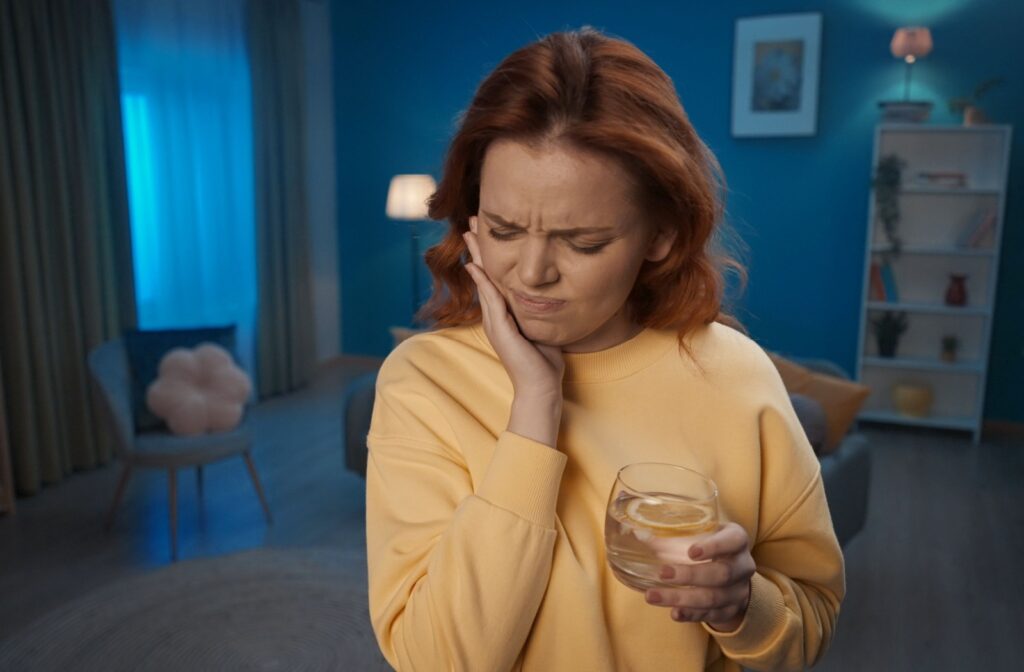 A woman experiencing tooth sensitivity while holding a glass of lemon water.