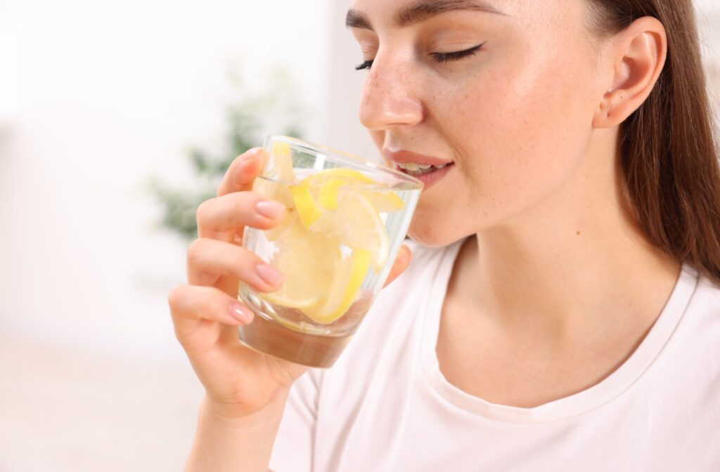 A woman sipping lemon water, which can lead to erosion, tooth sensitivity, and discolouration of the teeth.