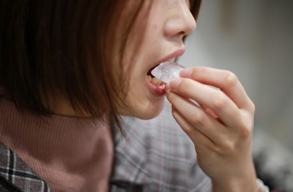 Close-up of a person chewing on a piece of ice, which can damage teeth and enamel.