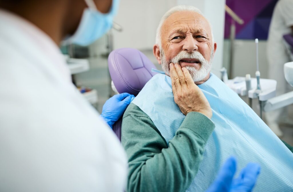 An older adult in a dental chair during a checkup rubbing their jaw and describing what their cracked tooth feels like.