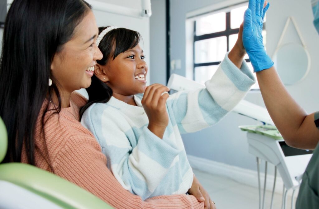 A child and her mother visit the dentist for her appointment and give the dentist a high five.