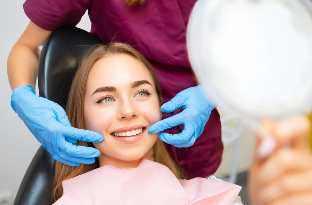 A patient at their dental recall exam, smiling into a handheld mirror