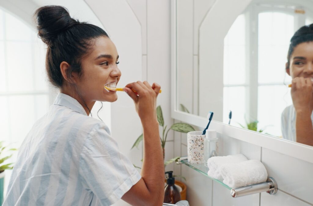 A person brushing their teeth in their bathroom to maintain good oral health.