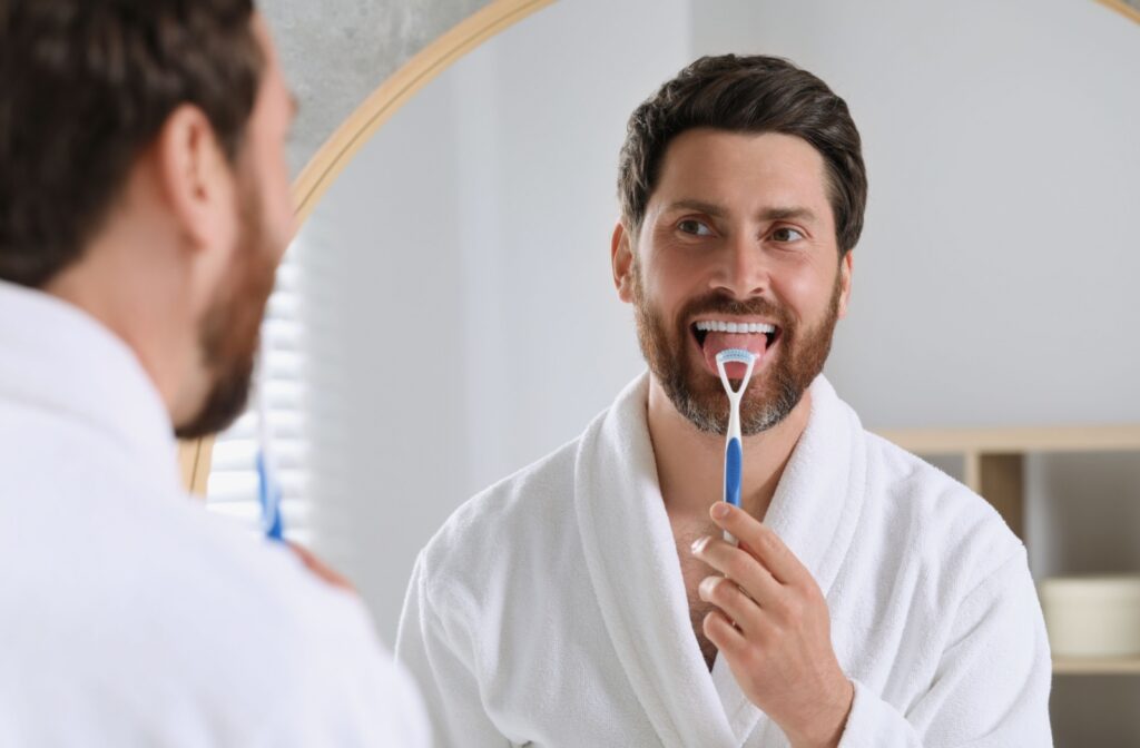 A person looking in a mirror using a tongue scraper to create a clean mouth feel.